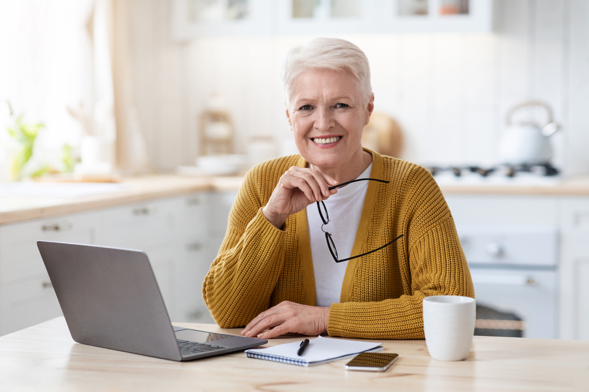 Smiling woman reviewing her finances on a laptop at her kitchen table